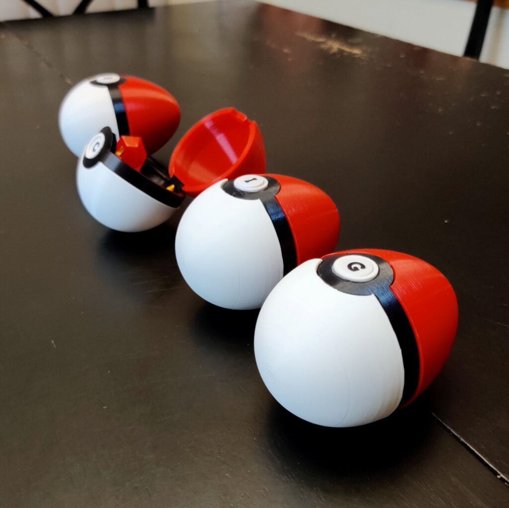 Poke balls shaped like Easter eggs sitting on a black table.